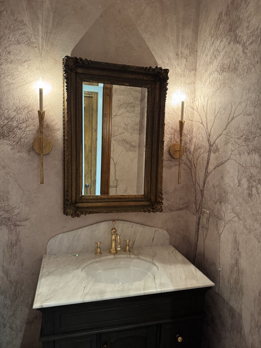 Gold candle-style wall sconces flanking a vanity mirror in a powder room